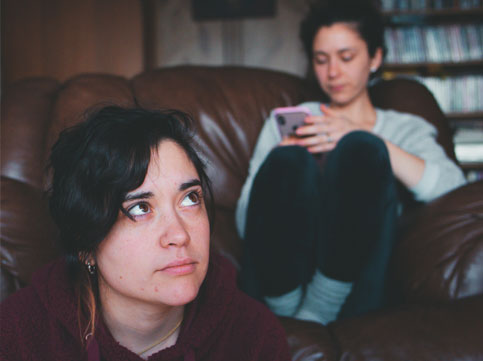 young person on the couch looking at her phone and another young person sitting down in front of the couch. family cancer