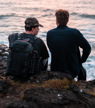 two males sitting on a rock by the ocean having a conversation. image for youth cancer services