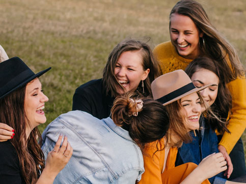 six female friends laughing and hugging each other at a park - image for youth cancer services