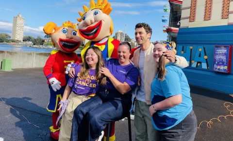 Four young adults in front of Luna Park with the Luna Park characters after one person shaved their head for Canteen's Bandanna Day