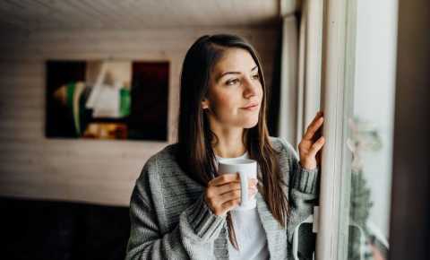 Young woman holding cup looking out window