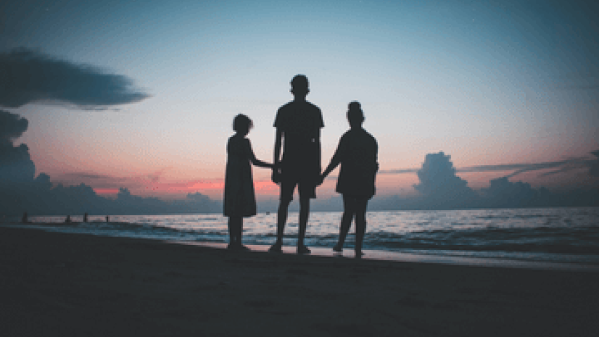 Three siblings hold hands on a beach