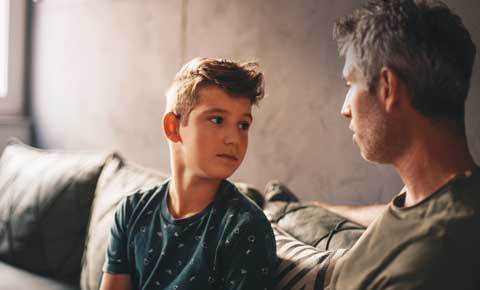 a son and father sitting on the couch talking to each other